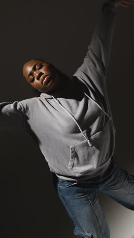 Vertical-Video-Full-Length-Studio-Portrait-Shot-Of-Young-Woman-Wearing-Hoodie-Dancing-In-Spotlight-With-Shadow